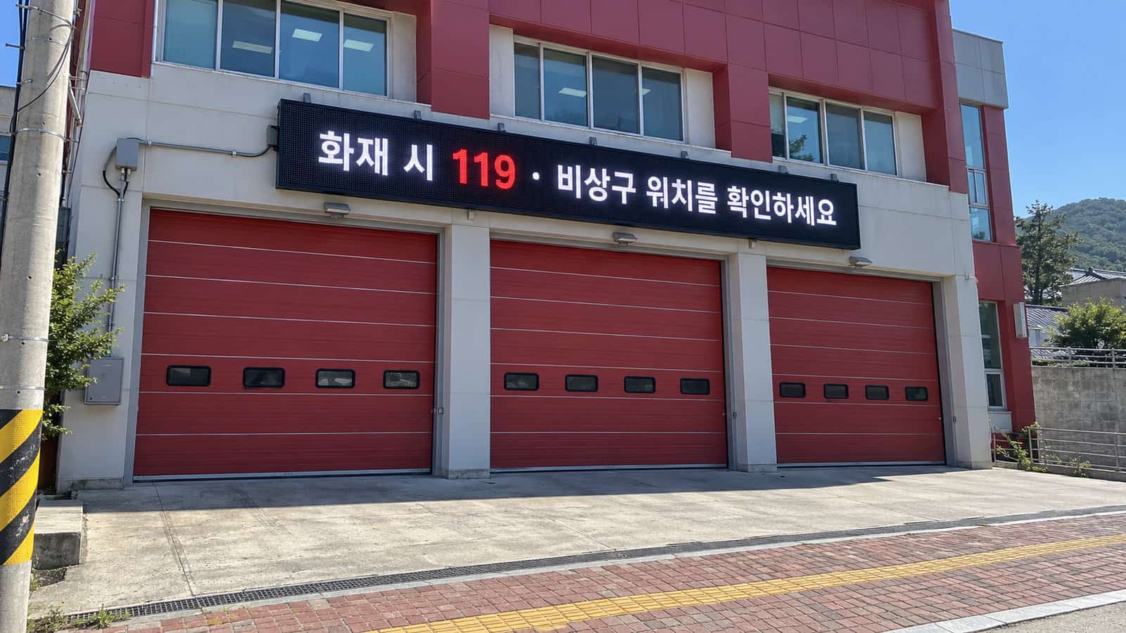 소방서 차고 출입문 위 외벽 LED 전광판에 화재 시 119 비상구 위치 확인 안내가 표시된 낮 장면