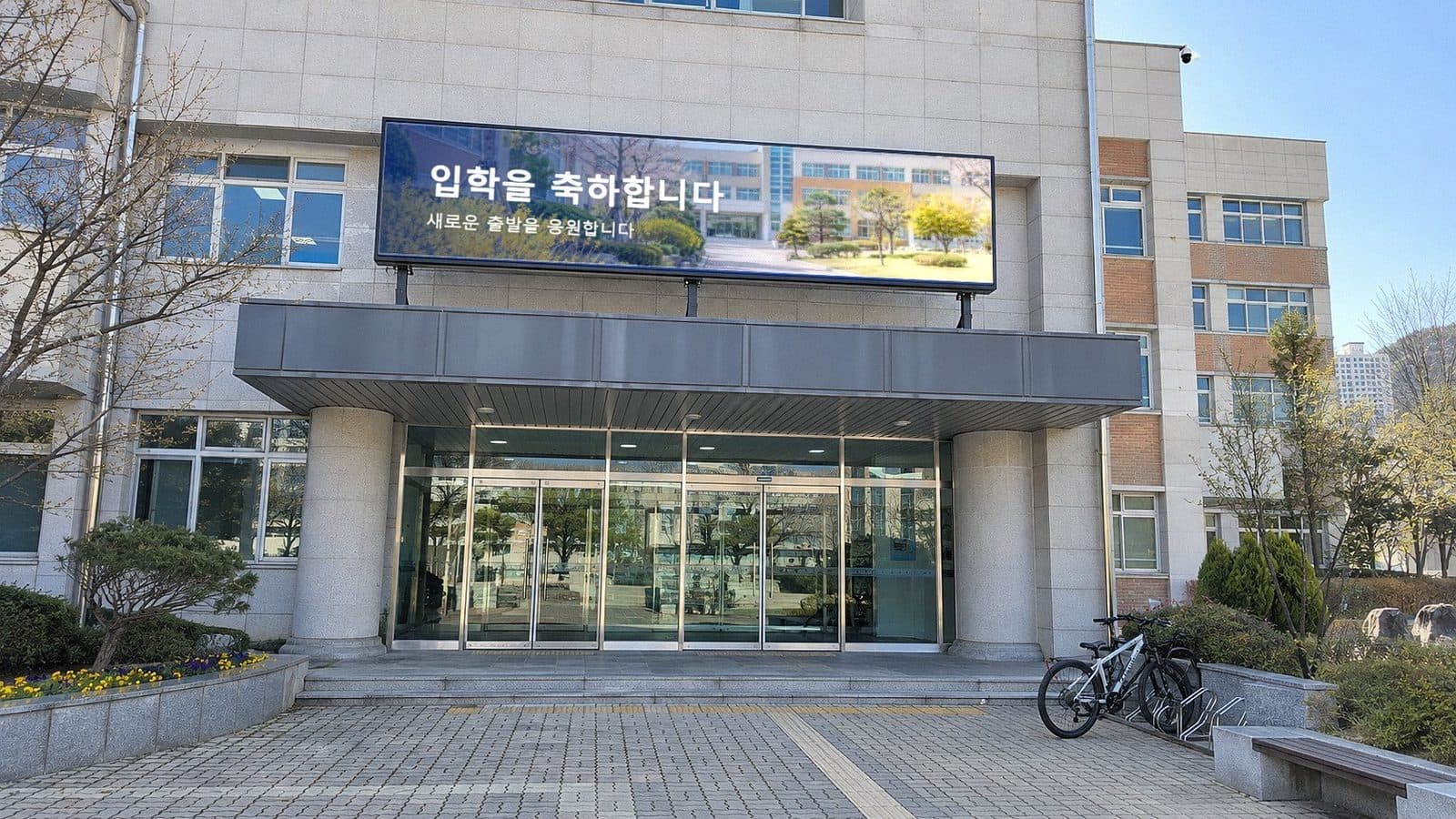 고등학교 본관 현관 캐노피 위 가로형 LED 전광판에 교정 사진과 입학을 축하합니다 문구