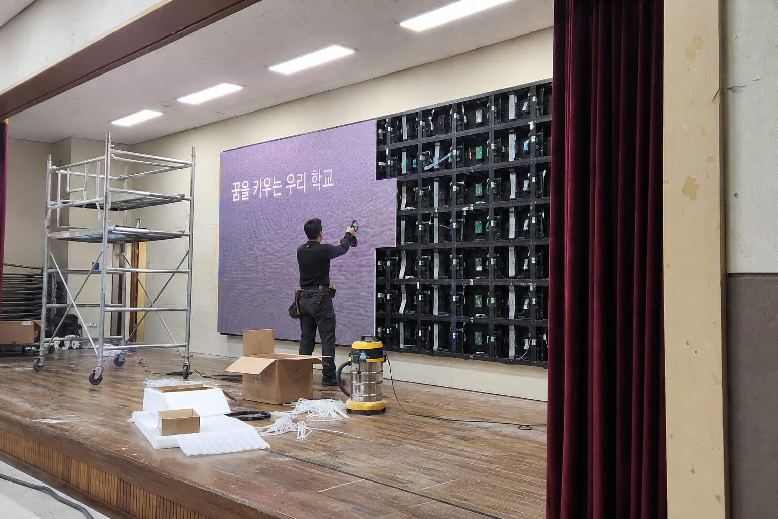 강당 벽면 프레임에 LED 모듈을 한 장씩 붙여 나가는 작업 장면