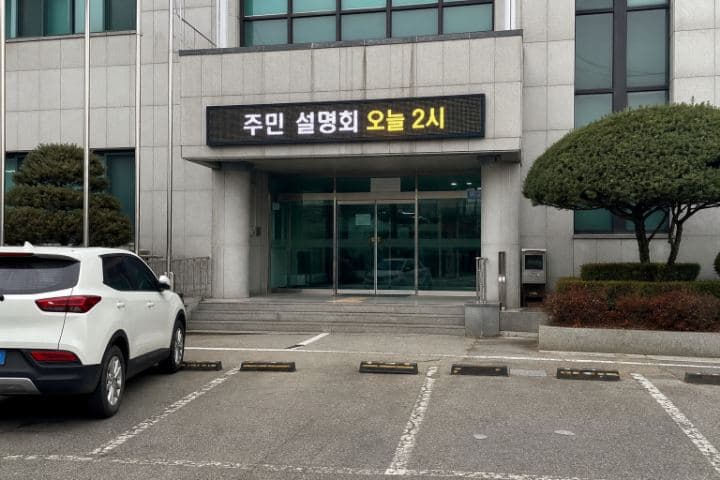 관공서 출입구 캐노피 위에 가로로 길게 설치된 LED 화면에 "주민 설명회 오늘 2시"가 표시되어 있다