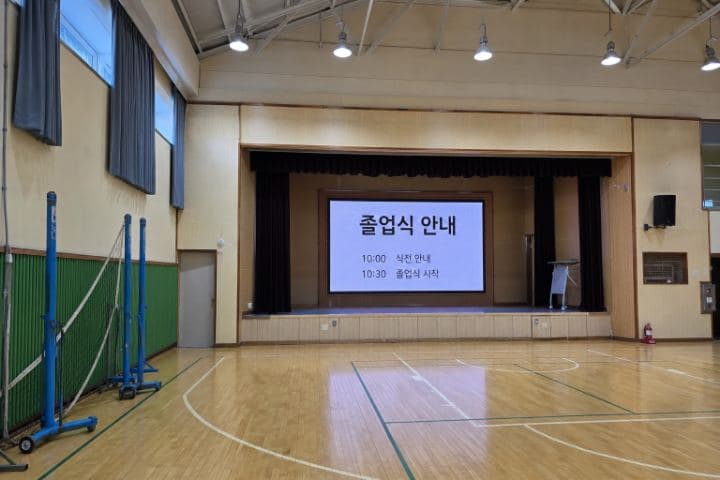 학교 체육관 무대 위에 설치된 화면이 졸업식 안내를 표시하고 있다