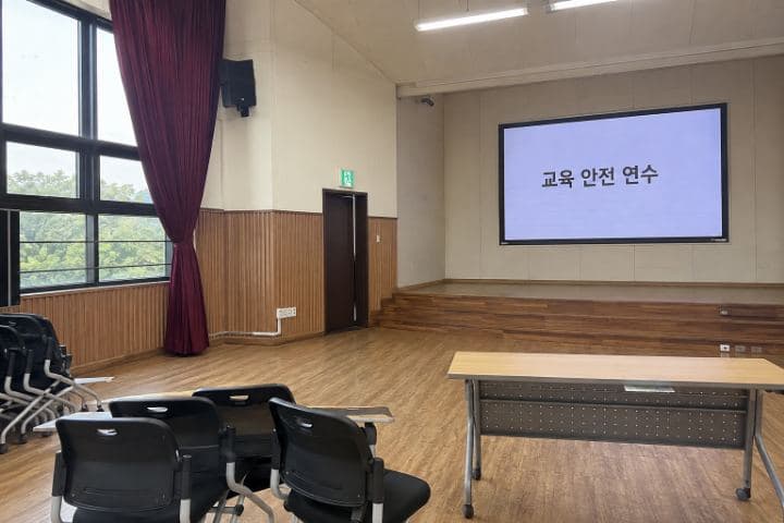학교 다목적강당 무대 벽면의 대형 실내 LED 화면에 "교육 안전 연수"가 표시되어 있다