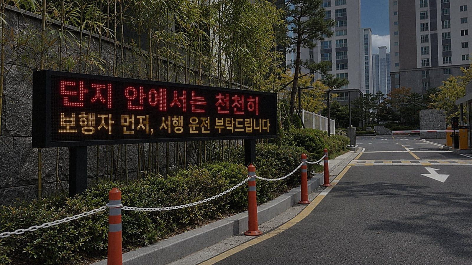 아파트 단지 진입로 옆 화단에 두 다리로 선 옥외 LED 글자 전광판에 단지 안 서행 안내가 나오는 장면